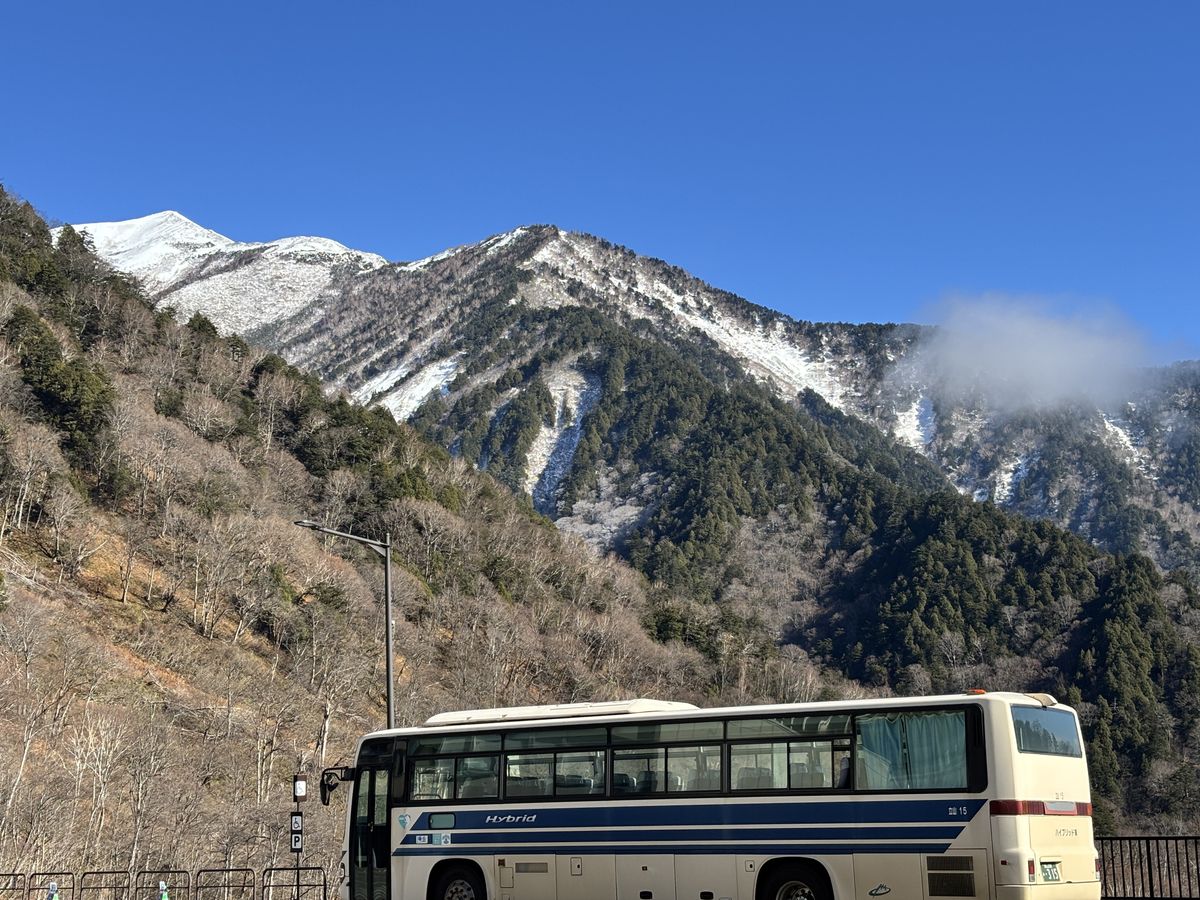 Hybrid bus waiting in the parking lot at Ogizawa Station, with snow-streaked peaks rising behind it