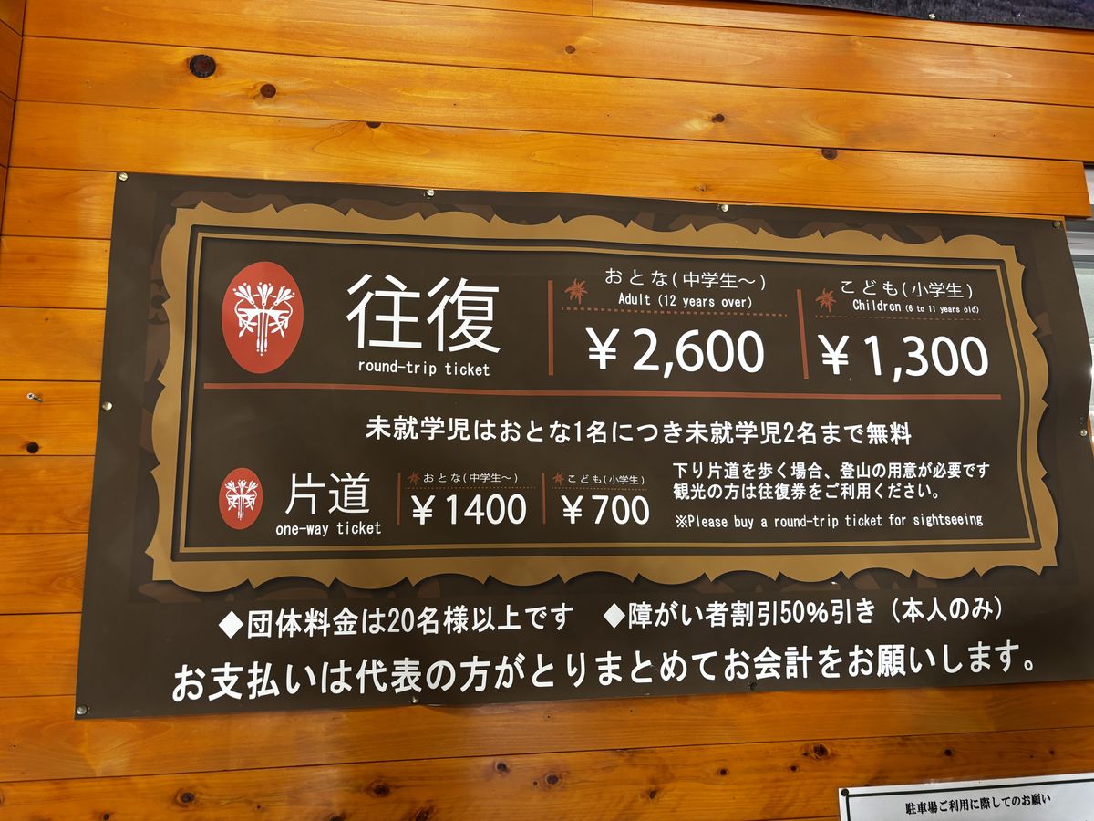 Fare board on a wood-panel wall showing 2,600 yen round trip and 1,400 yen one way for the ropeway