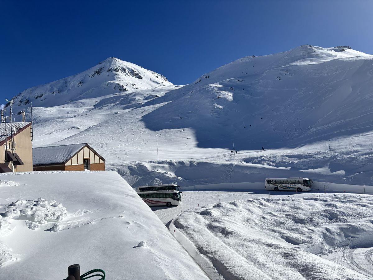 雪山の間を走る「ALPINE ROUTE」のバスと、青空の下に建つ立山黒部アルペンルートの施設