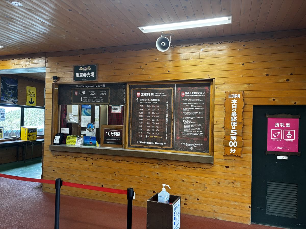 Ticket window, departure timetable and notice boards inside the wooden base station of the ropeway
