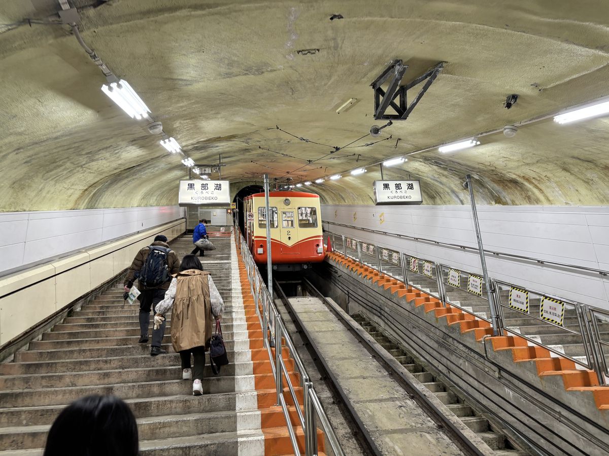 Passengers climbing the platform steps beside the red-and-cream cable car on the Tateyama Kurobe Alpine Route