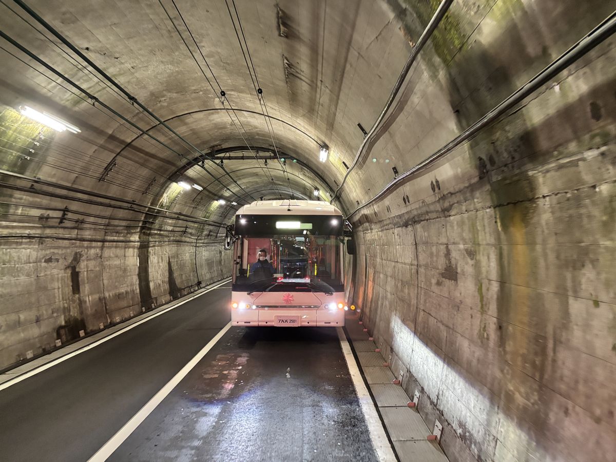 Pink electric bus approaching head-on through the concrete tunnel on the way up to Murodo