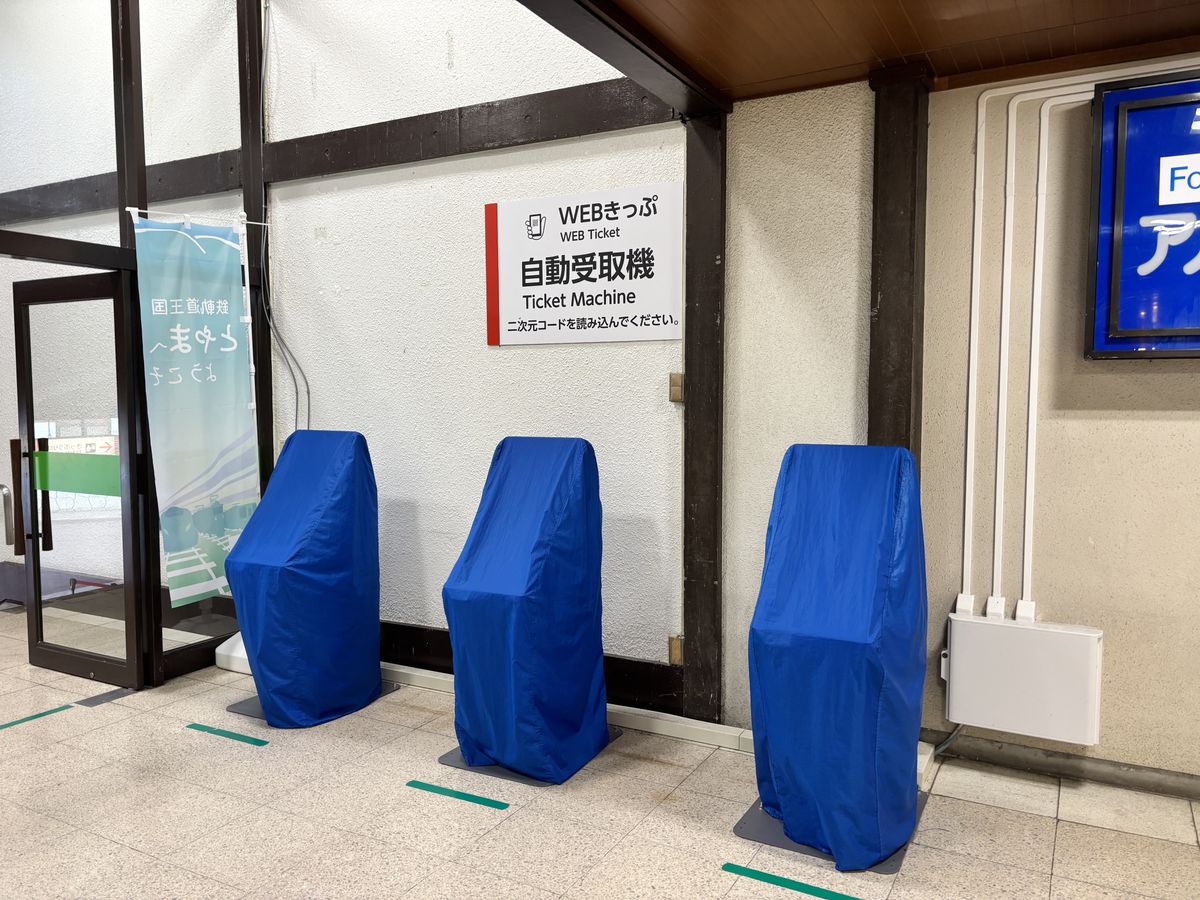 Three Web Ticket machines under blue covers in the station waiting area, a ticket information sign on the wall