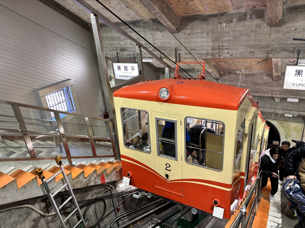 Travellers stepping off the orange-and-cream Kurobe Cable Car inside its tunnel station