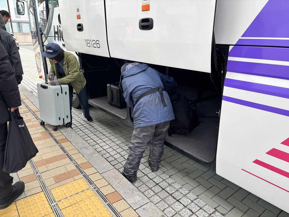 Passengers loading their suitcases into the underfloor luggage bay of an Alpico bus at the stop
