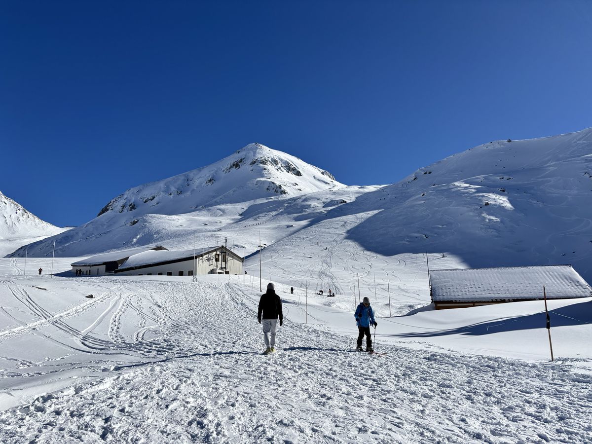 Two skiers standing by a hut on the snow field at Murododaira, a highlight of the Tateyama Kurobe Alpine Route