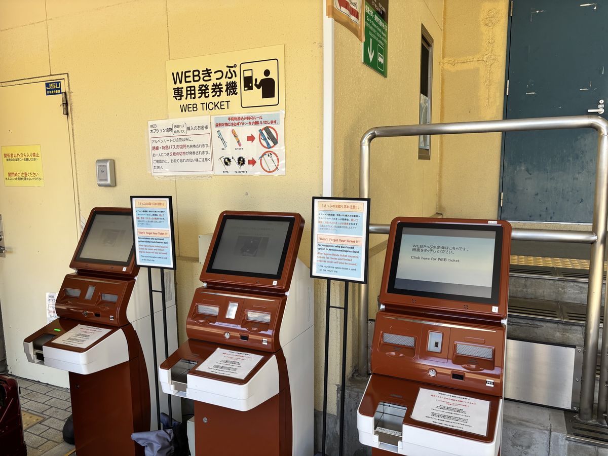 建物の壁際に3台並ぶWEBきっぷ専用発券機と、その上に貼られた案内表示