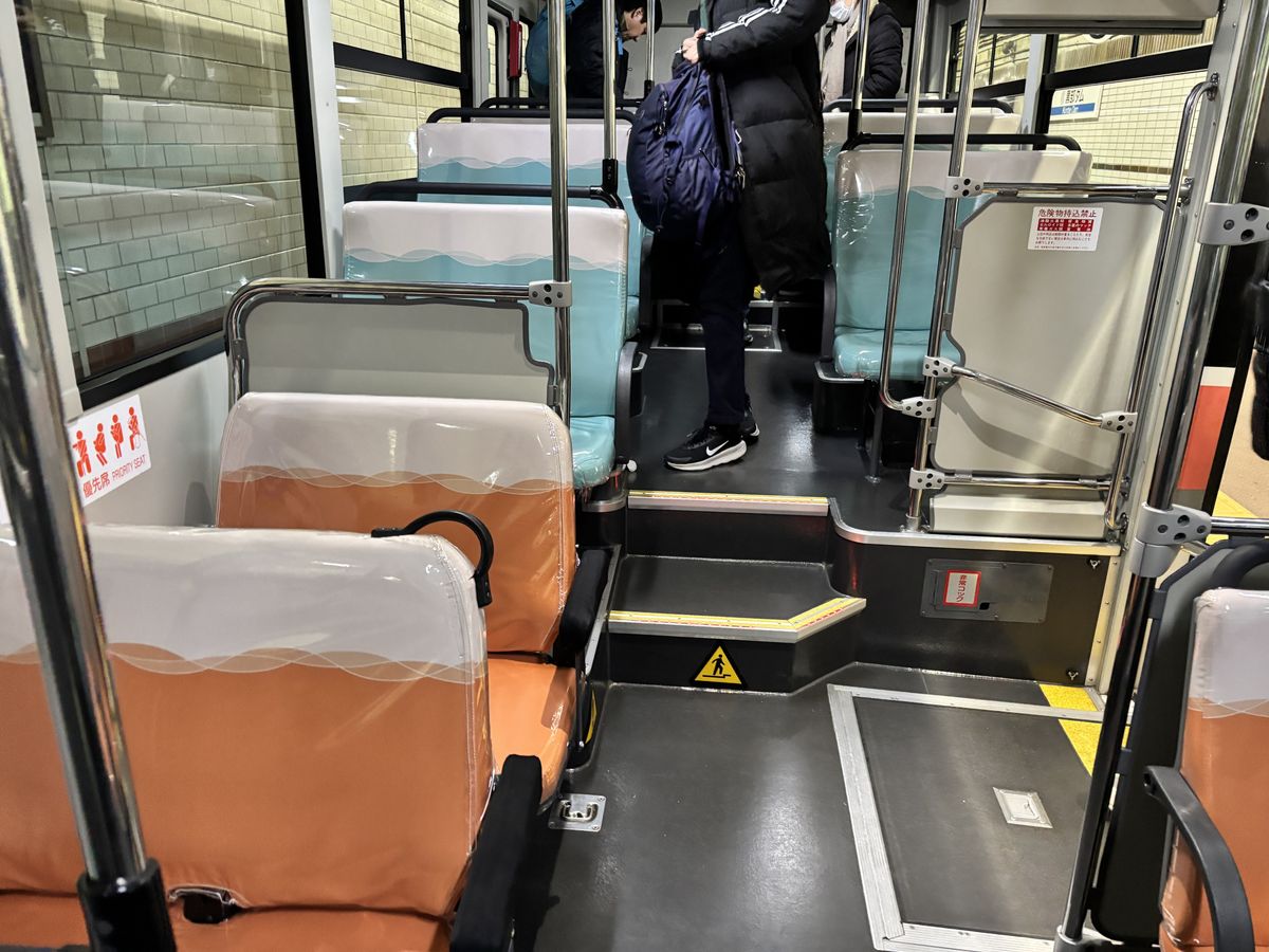 Inside the Alpico bus, a passenger in a thick coat moves down the aisle past seats wrapped in plastic covers