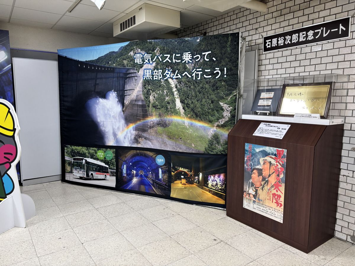 Indoor exhibit corner with Kurobe Dam photo posters, a film poster and a commemorative plaque on display
