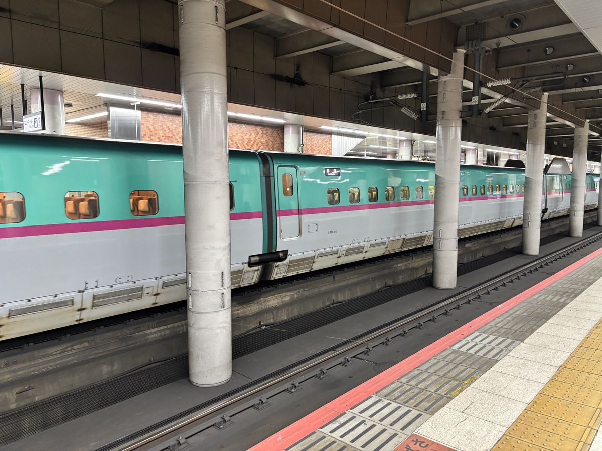 Hokuriku Shinkansen train, striped in green and pink, standing at the station platform before departure
