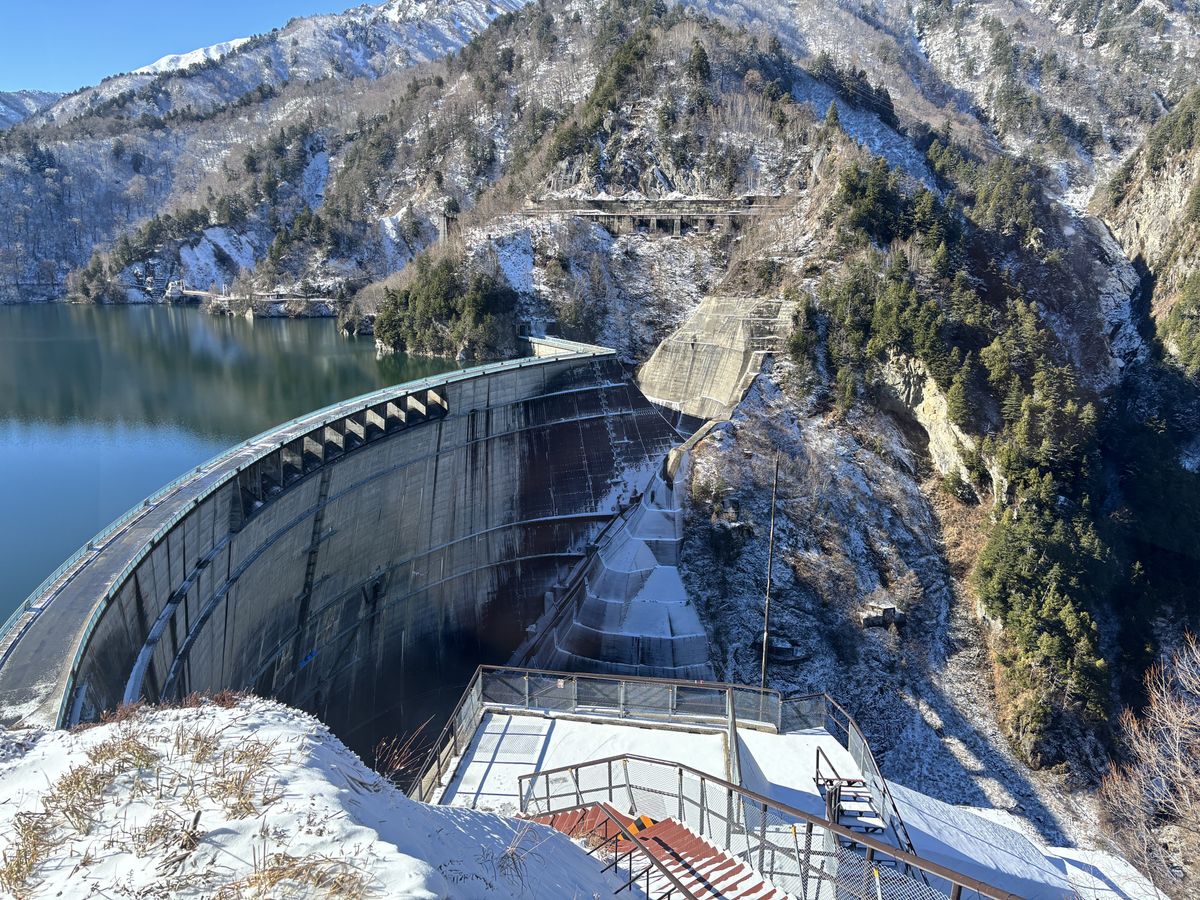 Panorama from the observation deck looking down on the dam and its lake, encircled by snow-capped mountains