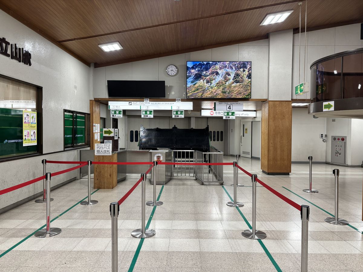 Empty boarding hall at Bijodaira Station, lined with direction signs and red rope partitions