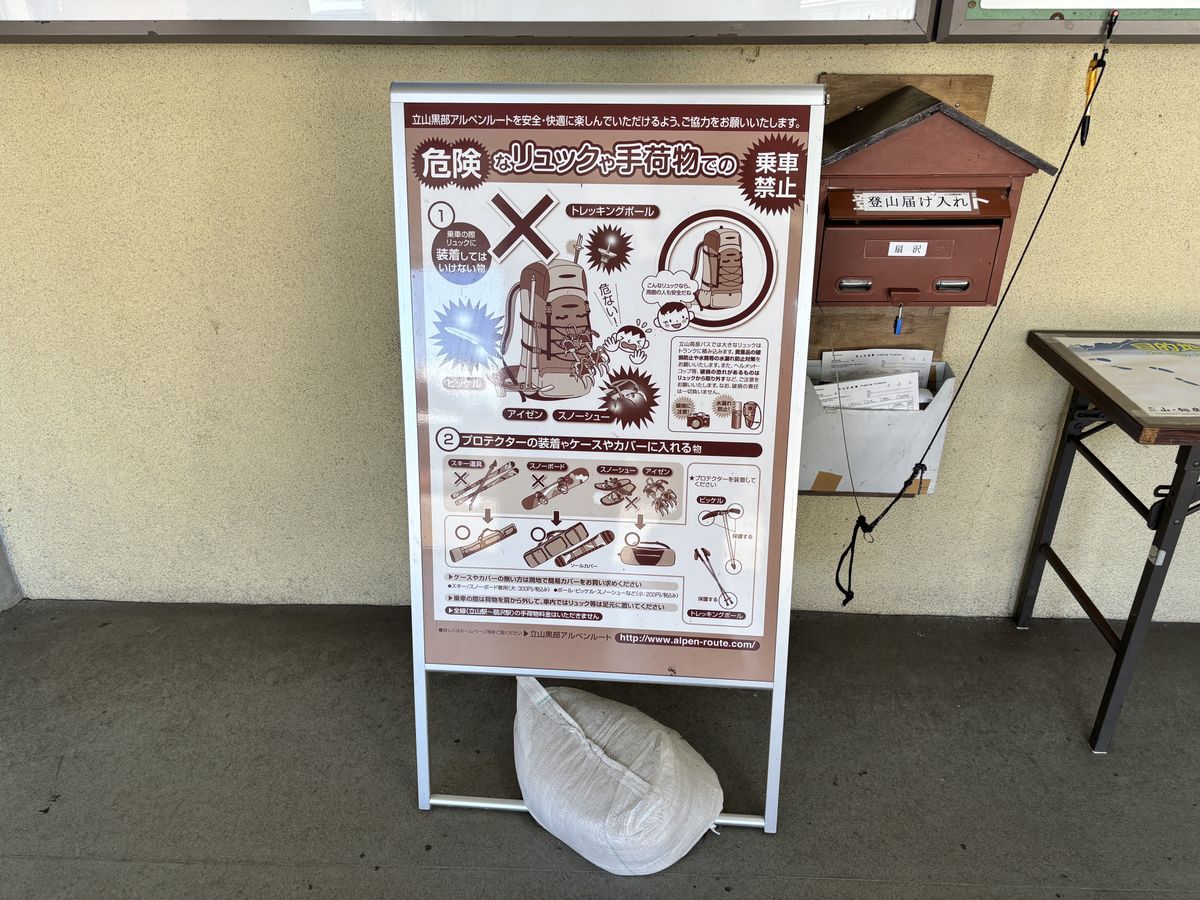 Drop box for climbing registration forms beside a luggage notice board under the eaves of an Alpine Route station