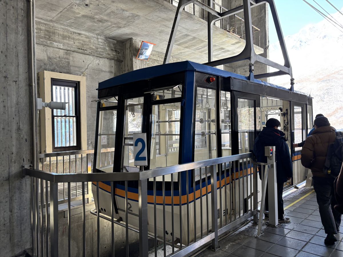 Passengers boarding a gondola at the Tateyama Ropeway station, snow-covered mountains filling the view